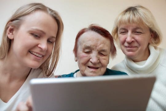 Smiling senior, daughter, and granddaughter on a computer.