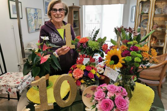 Senior woman with glasses celebrating her 101 birthday with flowers in her retirement suite