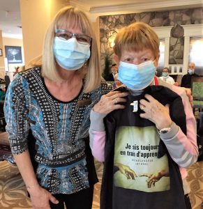 Deux femmes portant des masques, l'une tenant un t-shirt d'événement infiniment curieux.