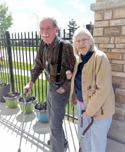 Senior couple walking arm in arm on a sunny day; man using cane; woman using a walking aid.
