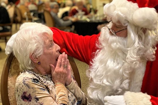 Santa Clause saying Merry Christmas to a surprised woman with short white hair