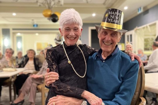 Older couple on new year's eve, woman with short grey hair sitting on lap of distinguished older man